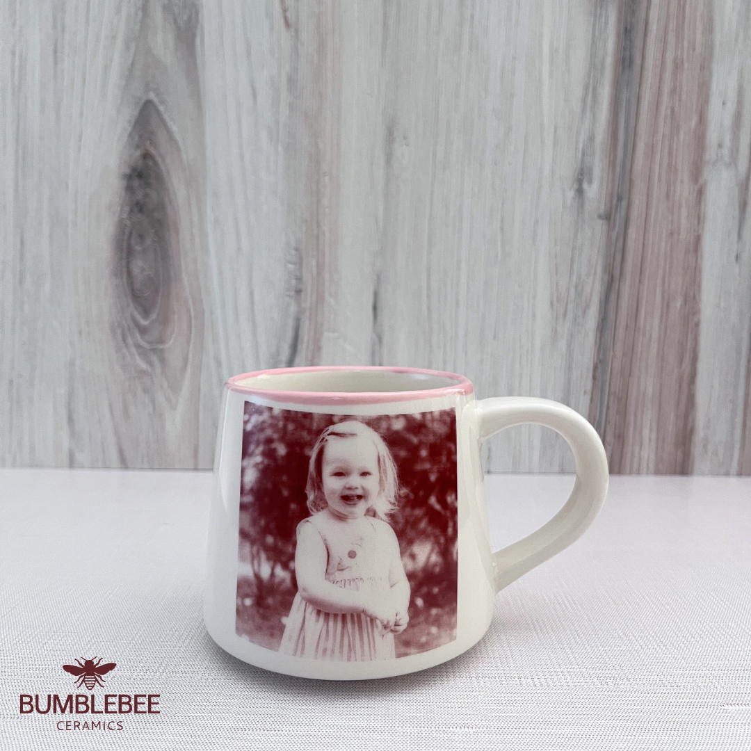 Mug with a printed photo of a child on a wooden surface, featuring the brand 'Bumblebee Ceramics'.